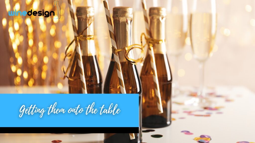 Mini champagne bottles tied with striped straws and gold ribbons on a table decorated with confetti and champagne flutes.